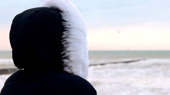 女人在冬季夹克与兜帽看大海黎明前特写