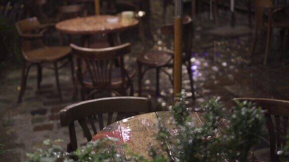 大雨夜里的街头咖啡馆湿木家具桌椅雨点落在桌上晶莹剔透雨中古老的欧洲户外咖啡馆植物在前台