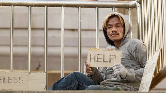 一个无家可归的人坐在立交桥上手里拿着救命的牌子