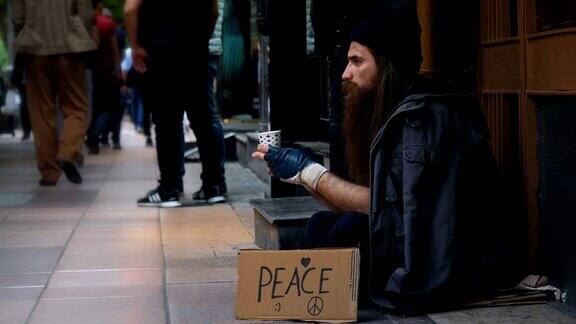 无家可归的人拿着“和平”纸板在拥挤的街道上乞讨