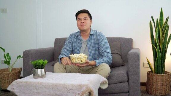 4k视频的亚洲人看电视喜剧电影或体育和吃爆米花享受在家里的沙发上