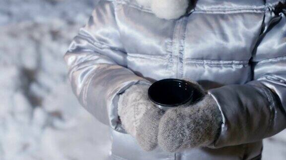 戴手套的小女孩在雪地上拿着茶杯