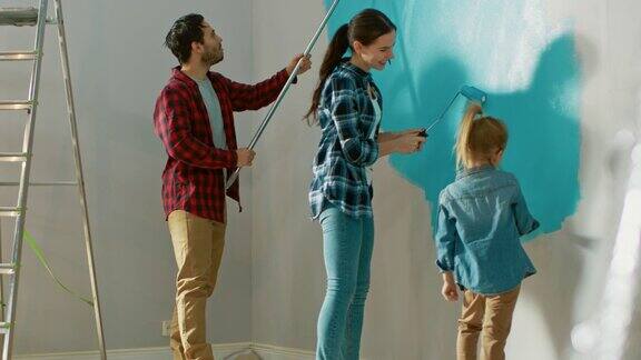美丽的年轻家庭正在给他们可爱的小女儿展示如何刷墙他们用涂有浅蓝色油漆的滚筒来作画室内装修