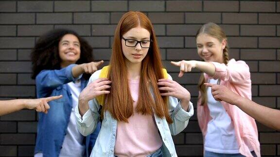 十几岁的孩子们用手指逗弄戴眼镜的新聪明同学书包