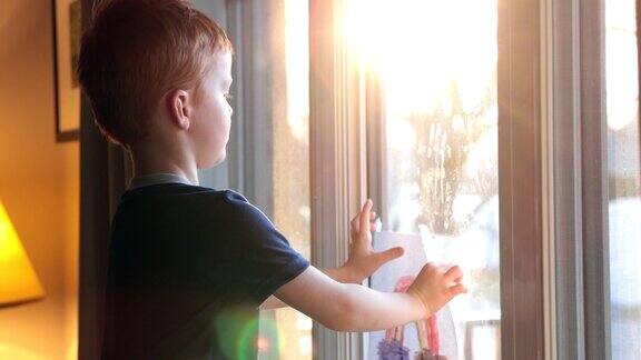 2019冠状病毒病危机期间小男孩在自家窗户上贴彩虹画