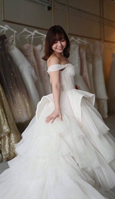 快乐骄傲满意的亚洲中国新娘肖像摆姿势看着相机微笑在婚纱店试婚纱长大