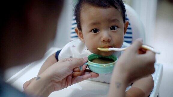 亚洲母亲在家用勺子喂儿子的照片