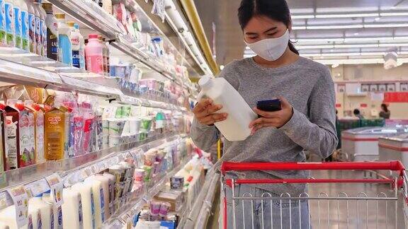 年轻的亚洲女性带着防护口罩在超市购买日用品她正在阅读写在包装上的产品信息