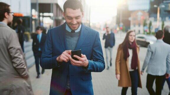 西装革履的白人商人正在市中心的一条街上使用智能手机办公室里的其他人走过他微笑着看起来很成功他在用他的设备浏览网页
