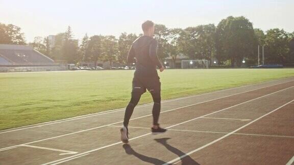 运动健美男子在灰色衬衫和短裤在体育场慢跑在一个温暖的夏日午后他正在舒服地跑步运动员在做例行运动练习跟踪拍摄