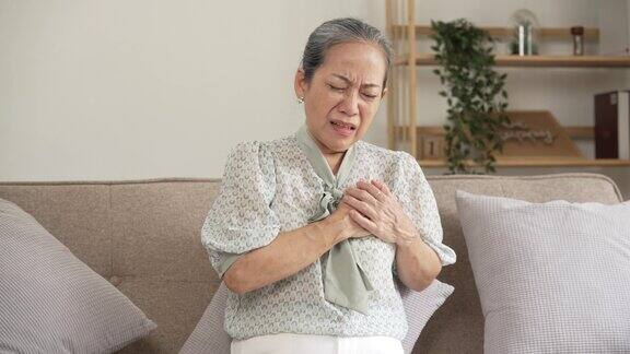 成熟的亚洲女性心脏病发作坐在沙发上
