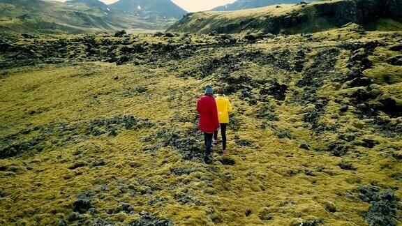鸟瞰图两名女性行走在覆盖着苔藓的火山岩上在冰岛探索草地游客一起徒步旅行