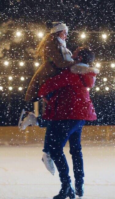 垂直视频浪漫的冬夜:滑冰情侣在溜冰场玩得很开心美丽的雪落在双人滑冰男朋友和女朋友在爱舞蹈牵手拥抱花样滑冰
