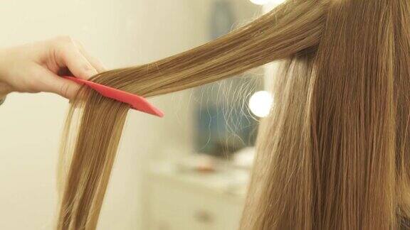 发型师在美发厅用夹子梳理长发并拉直近距离观察女性发型师在美容院做头发的过程