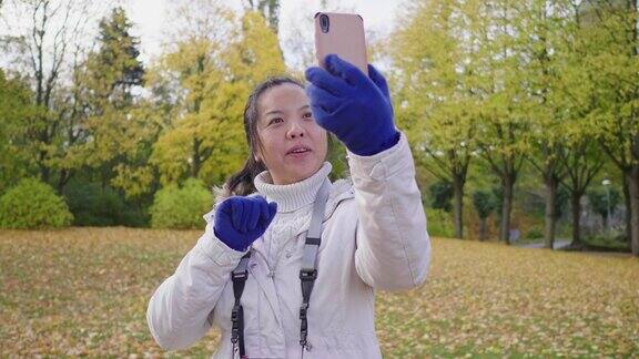 快乐的亚洲女人在秋天在公园视频通话