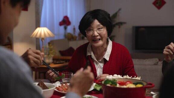 在家庭团圆饭期间一位身着红色衣服的快乐的亚洲老年妇女祖母与她的成年儿子在餐桌上用手势交谈