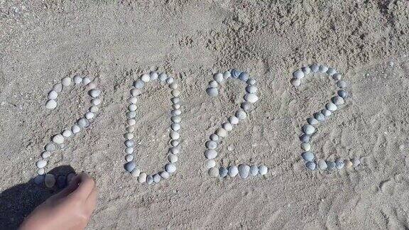 女孩的手从海边的贝壳上摊开数字“2022”