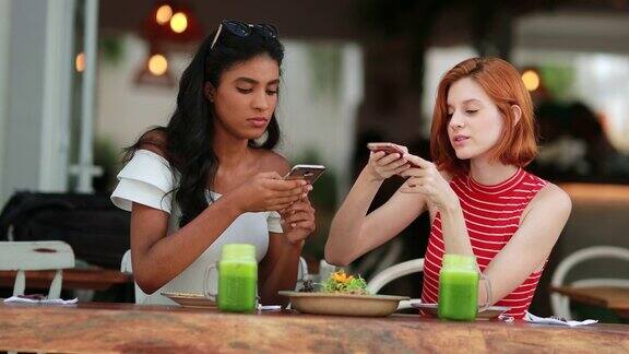 来自不同文化的女孩用手机拍照女性朋友坐在餐厅