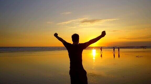 慢镜头:日落时分一名快乐的游客高举双手在海滩上旋转