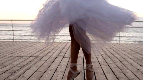 年轻的芭蕾舞女演员的腿在舞蹈动作的近距离镜头芭蕾舞者穿着白色短裙在户外练习木地板白天