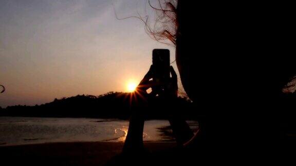 一名女子用智能手机在日落时分的海滩上拍照
