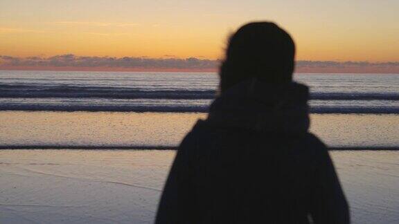 在日落时看海滩宁静的海浪的女人
