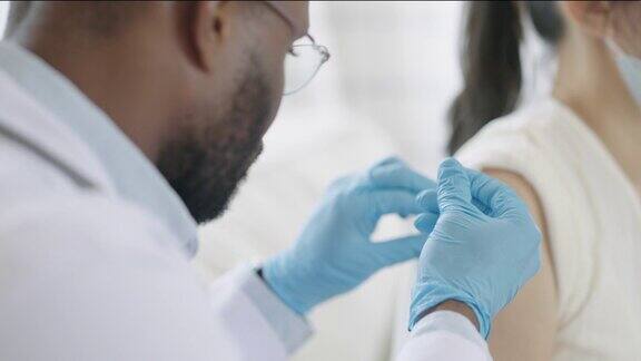 非裔美国男医生或护士在医院或家中为女性患者的肩部注射或接种疫苗以预防冠状病毒大流行COVID-19疫苗