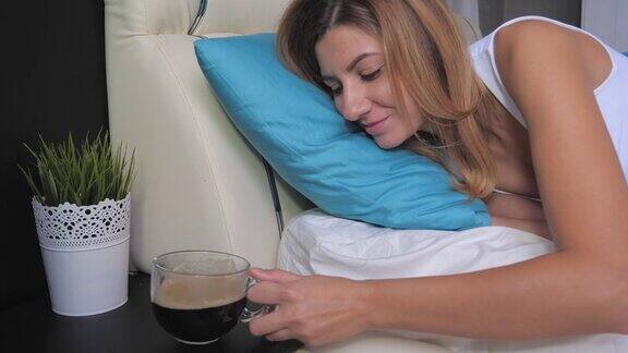 女人在床上醒来伸手去拿床头柜上的咖啡和饮料