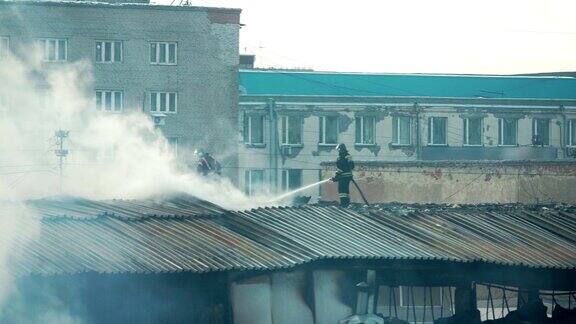 消防队员或消防队员在梯子上用烟扑灭公寓屋顶上燃烧的火焰