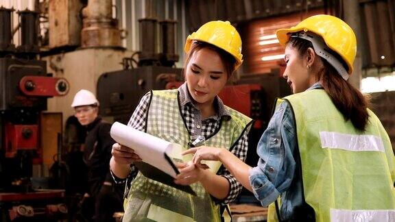 两名工厂女工程师与工人一起在检查机器交谈和检查生产报告背景