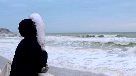 在日出前穿着冬大衣戴着头巾的女人看着大海慢镜头