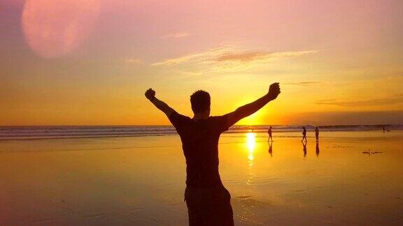 慢镜头:日落时分快乐的旅行者举起双手在海滩上旋转