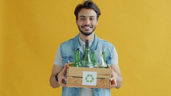 一名中东男子手持装有回收标志的玻璃瓶盒子的慢镜头肖像