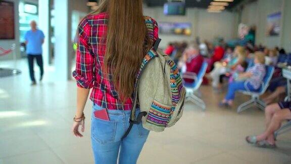 年轻的女游客女游客穿着休闲衬衫带着行李走在机场候机厅从后面看