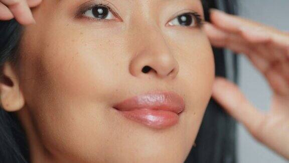 美丽的亚洲女人触摸她完美的脸女性享受她的美丽高自尊和健康天然化妆品护肤品提升孤立背景的特写肖像