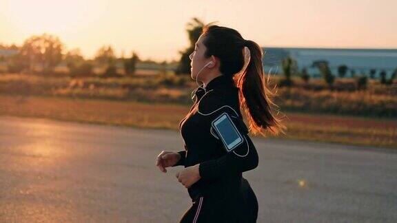 戴着耳机的女人在夕阳下奔跑时间(慢镜头)