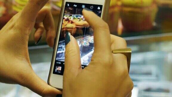 一个女人的手的特写正在面包店用智能手机拍摄面包房的图片
