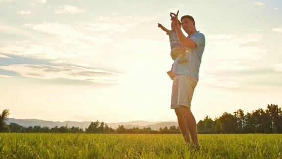 日落时分父亲抱着蹒跚学步的儿子在草地上