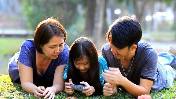 快乐的亚洲家庭一起在公园玩智能手机游戏