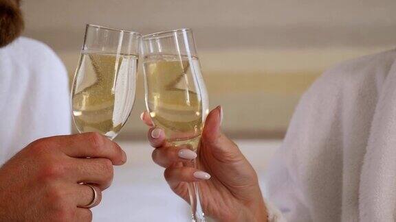 一对夫妇在浴衣与香槟在酒店房间碰杯的特写