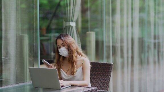 商业女性作为自由职业者使用笔记本电脑使用智能手机戴口罩