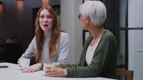 一个年轻的女人在家里喝着咖啡和她年迈的母亲聊天老太太在家里和女儿聊天喝茶