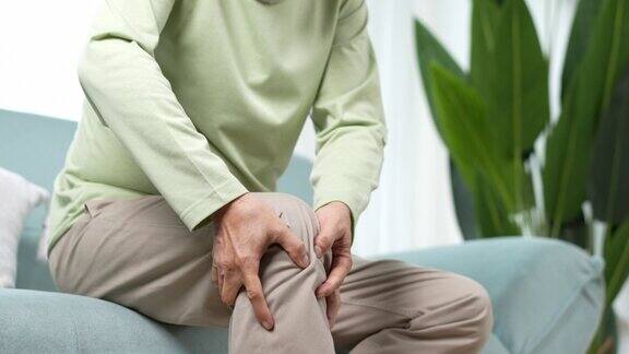 亚洲年长男子感到膝盖疼痛疼痛年长的成年男性坐在家里客厅沙发上时膝盖受伤骨骼问题保健与医疗保险概念
