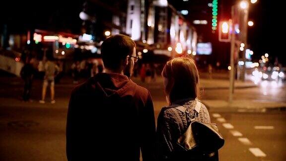年轻时尚的夫妇站在等待红绿灯的背影美丽的男女在傍晚过马路