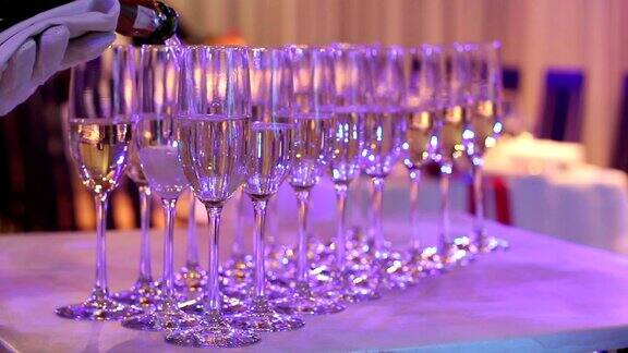侍者将香槟倒入玻璃杯中香槟玻璃杯放在自助餐桌上餐厅或酒店的大厅里侍者的手上戴着白手套拿着一瓶香槟室内特写