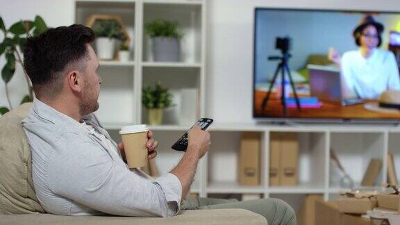 坐在电视机前用纸杯喝咖啡的男人