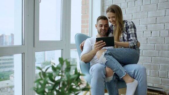 年轻愉快的夫妇在现代阁楼公寓的阳台上聊天和使用平板电脑