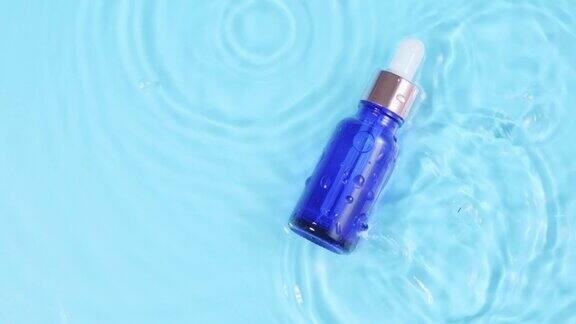 广告慢动作玻璃化妆瓶与吸管躺在水面上俯视水滴落入水中蓝色背景上发散的水圈包装设计