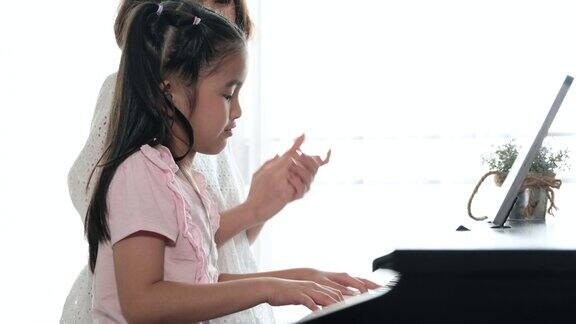 亚洲母亲和她的女儿一起弹钢琴的慢镜头母亲带着幸福和微笑拍着手教女儿