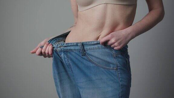 减肥和身体形象概念年轻女子穿着旧牛仔裤展示她的减肥成果穿着大牛仔裤的苗条女孩展示了当她开始吃健康食品时她是如何减肥的
